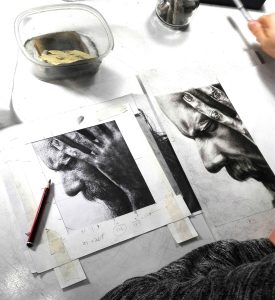 Retrato en grafito de una persona con barba y manos en la frente, en proceso de dibujo en una escuela de arte en Barcelona.