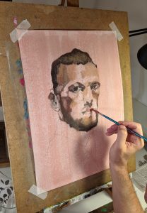 Retrato en proceso de un hombre joven, manos en acción pintando detalles en lienzo rosa, en la escuela de arte en Barcelona, centrado en dibujo y pintura.